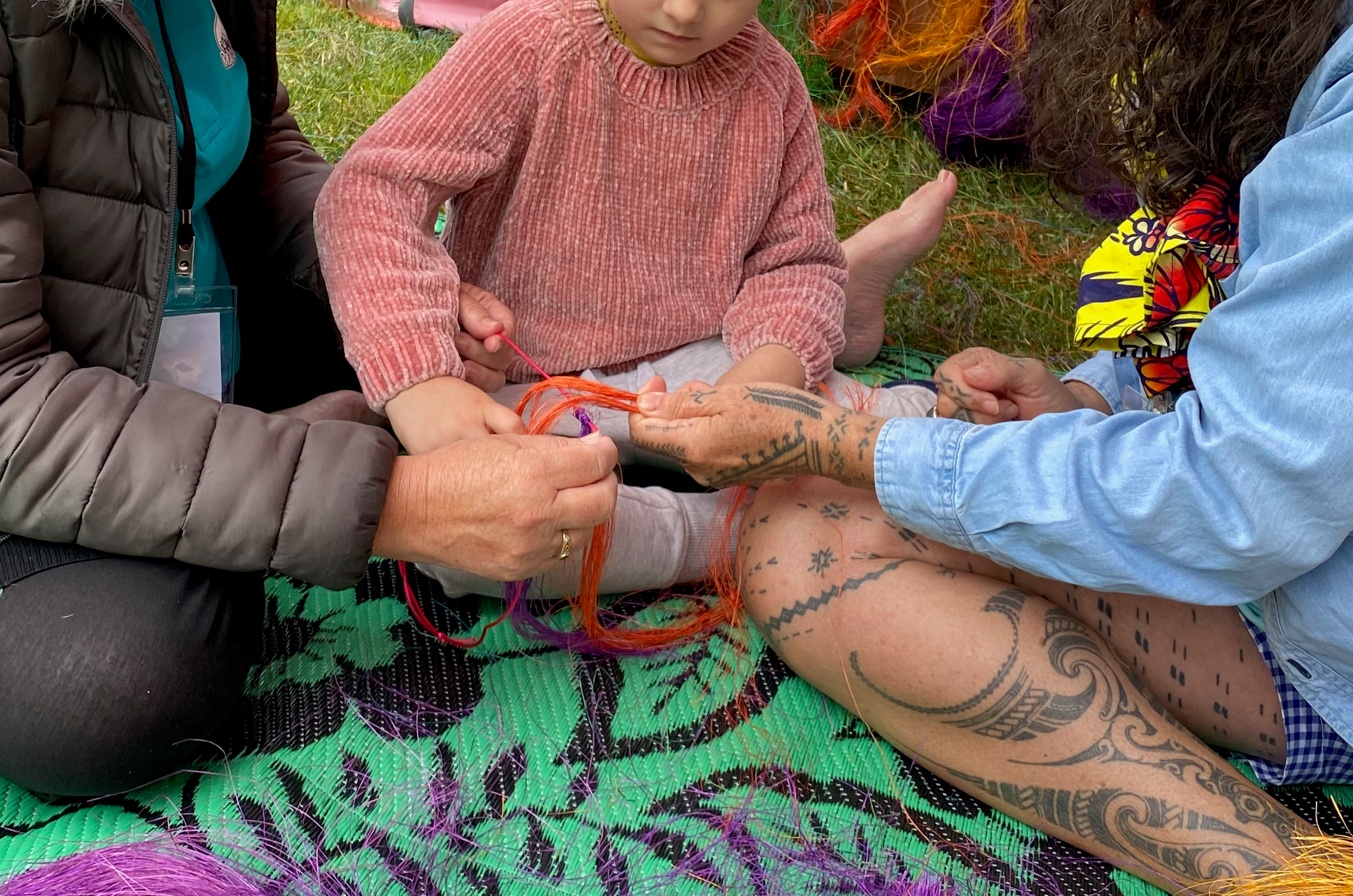 two adults and a child working together on weaving yarn