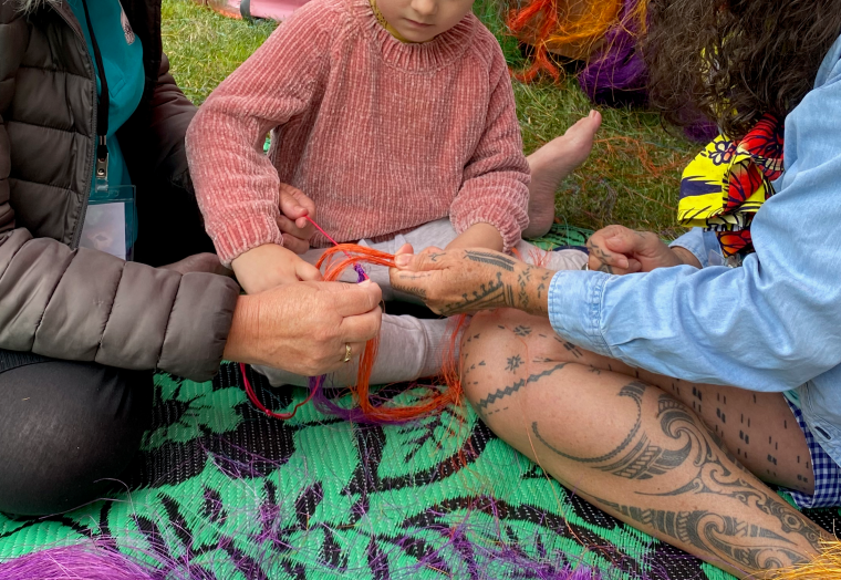 two adults and a child working together on weaving yarn