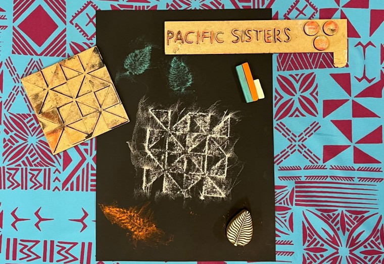 Flat lay of black paper with soft pastel rubbings that depict pacific sisters text