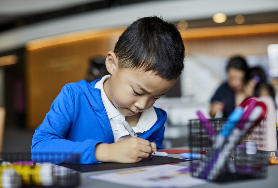 A young child in a blue jacket completing a drawing.