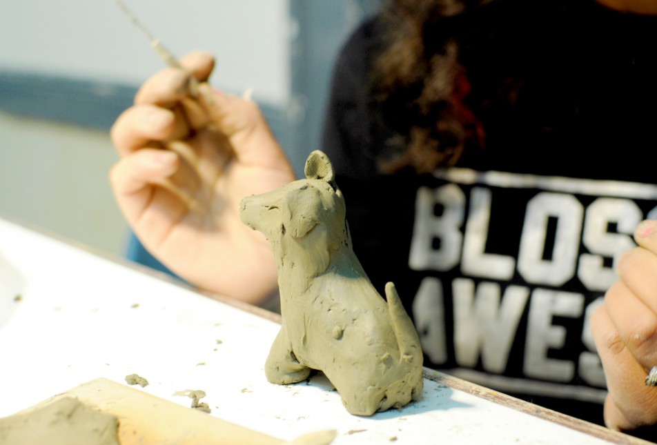 A person wearing a black t shirt crafting a four-legged creature from clay.